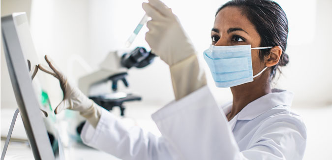 A researcher looks at a vial while working in a lab.